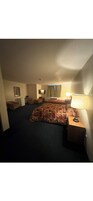 Quarto de hotel com uma cama grande, uma escrivaninha, uma cadeira, um abajur, uma televisão e uma janela com cortinas.