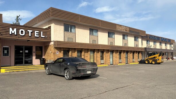 A motel with a signboard, a black car parked in front, and a yellow vehicle on the right. - Cataline Motor Inn (Fraser Lake)