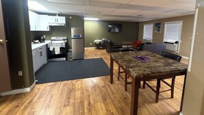 A room with a kitchen area, a dining table, and a black carpet. - Cataline Motor Inn (Fraser Lake)