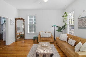 Ein Wohnzimmer mit Couchtisch aus Holz, zwei Sofas, einem großen Spiegel und einer hängenden Pflanze.