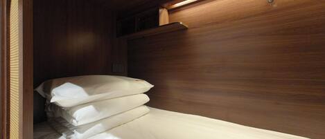 A compact, wooden interior with a single bed, a small shelf, and a wall-mounted light fixture.