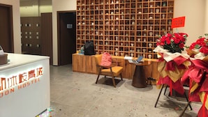 En hotellobby med en hylla i trä där olika föremål visas upp, en incheckningsdisk, en sittgrupp med en stol och ett bord samt en skylt som visar hotellets namn.