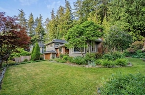 Ein zweistöckiges Haus mit gepflegtem Rasen und dichtem Wald im Hintergrund.