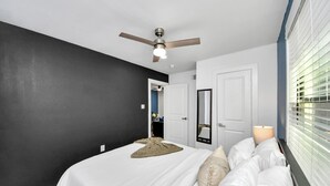 Ein Schlafzimmer mit Bett, Deckenventilator, Fenster mit Jalousien und einer Tür.