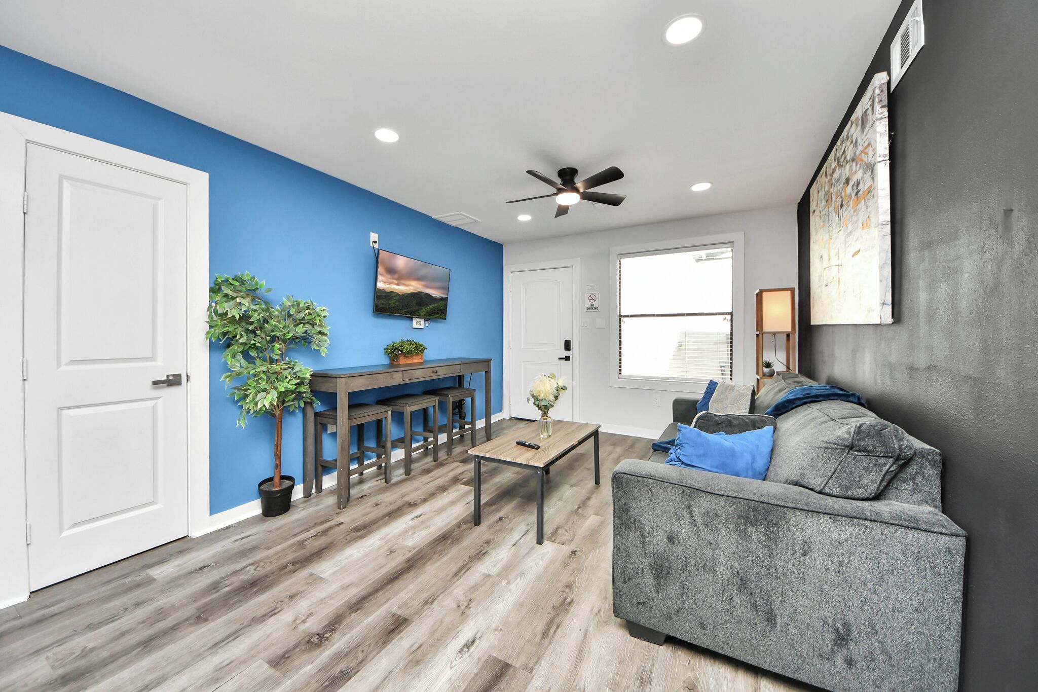 A living room with a gray sofa, a coffee table, a TV, a ceiling fan, and a dining area with a table and chairs.