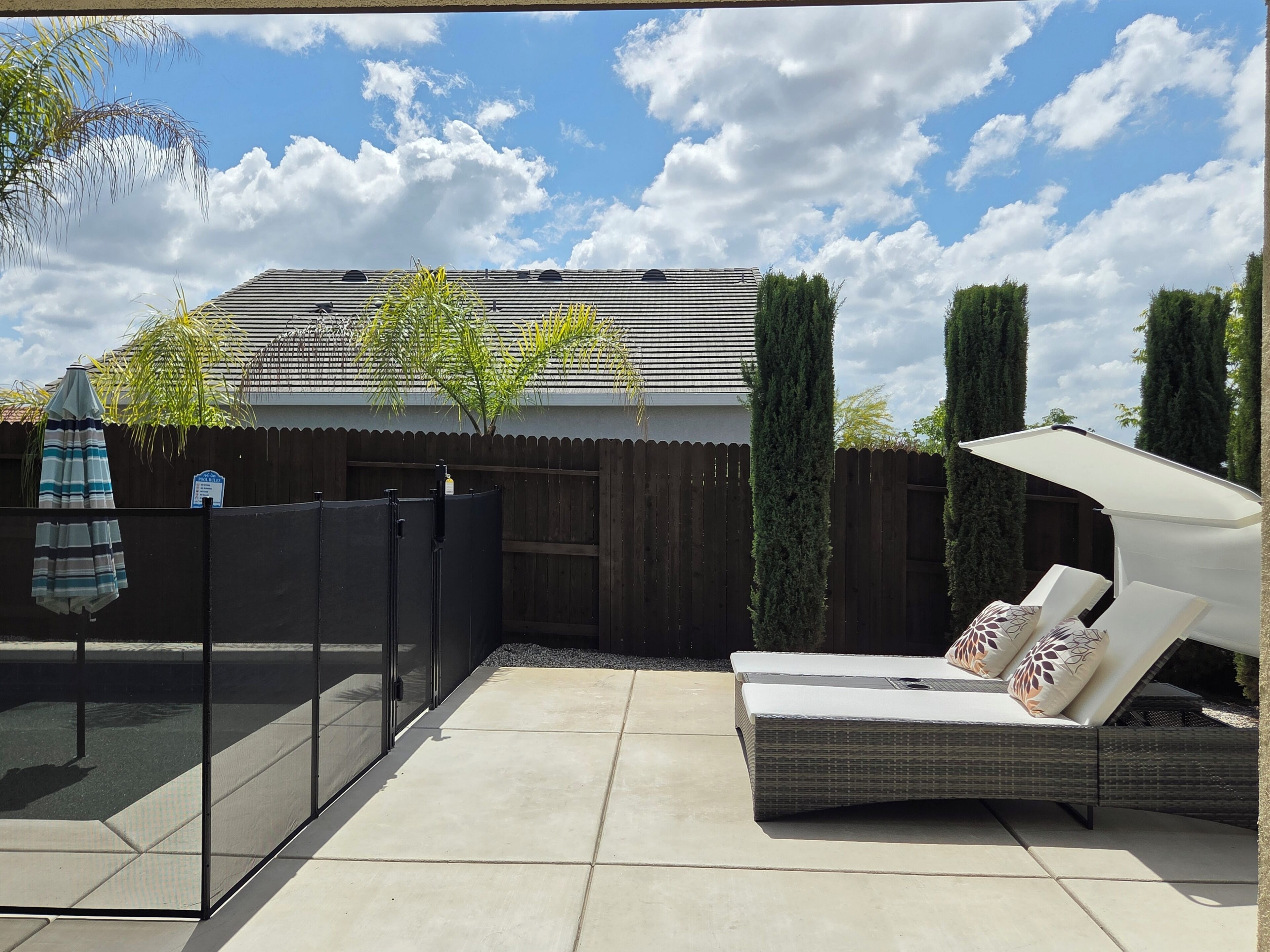 A patio with a glass enclosure, a white outdoor sofa, and a wooden fence.