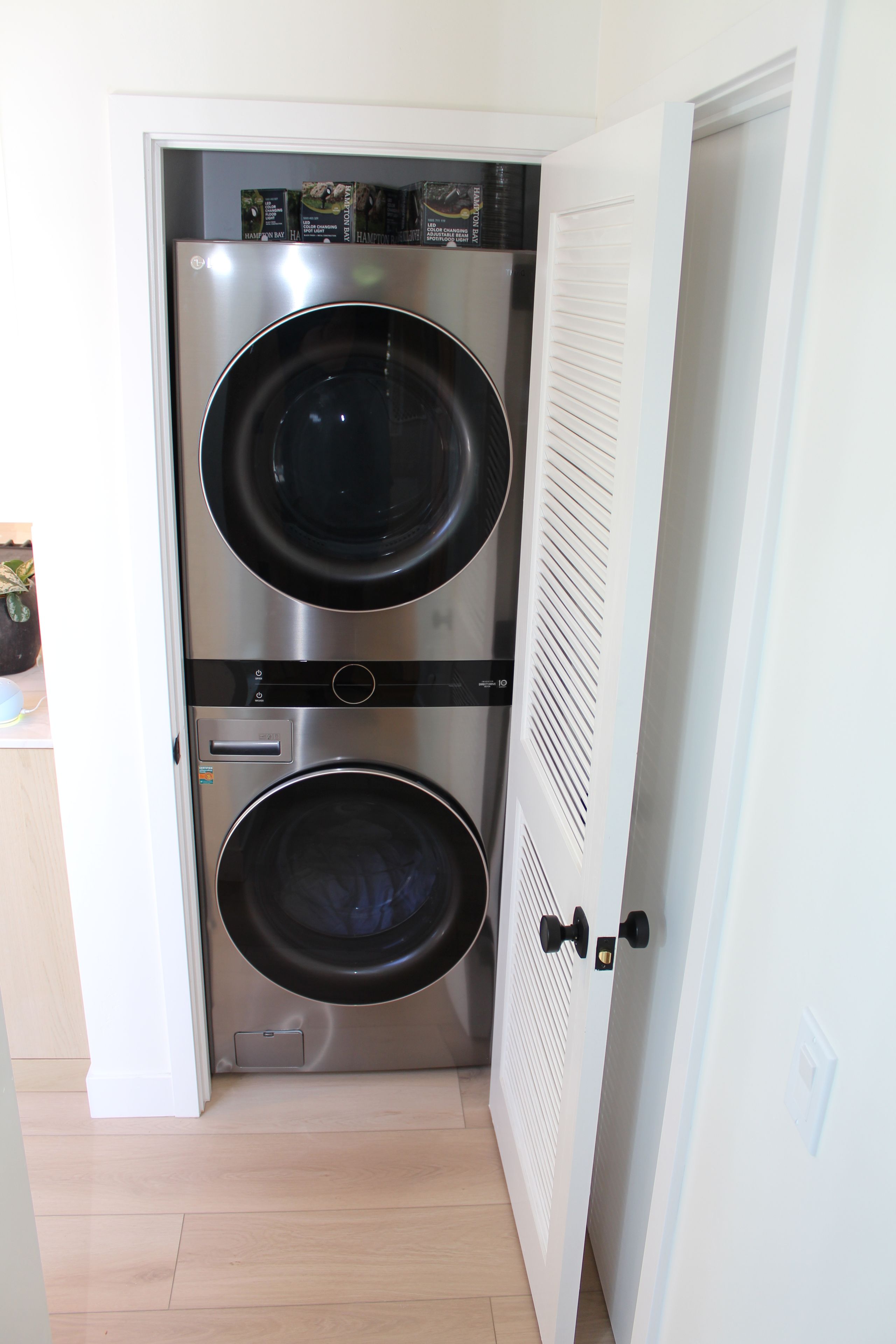 A compact, stainless steel washer and dryer unit installed in a narrow hallway with a white door.