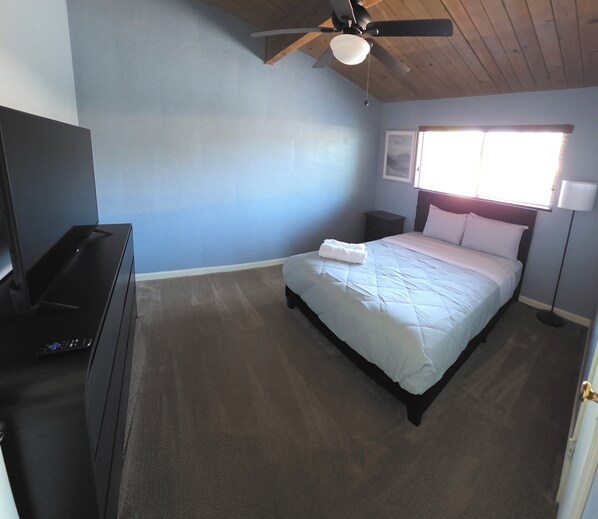 A bedroom with a bed, a ceiling fan, a nightstand, a lamp, and a TV.