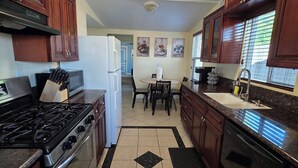 A kitchen with wooden cabinets, a stove, a refrigerator, a dishwasher, and a dining area with a table and chairs. - Wi-fi / Pool / Ac / Parking / Patio / Grill /Workspace / Ice Chest. (Bakersfield)