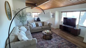 A spacious living room with a high ceiling, a large sofa, a coffee table, and a television. - Wi-fi / Pool / Ac / Parking / Patio / Grill /Workspace / Ice Chest. (Bakersfield)