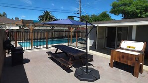 Un patio trasero con piscina, terraza de madera, mesa de picnic y zona de estar cubierta.