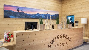 Un comptoir d’accueil en bois orné d’un tableau représentant une montagne, d’un téléviseur et d’une enseigne indiquant « SWISSPEAK RESORTS ».