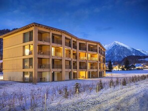 A multi-story hotel with balconies, a snow-covered ground, and a mountain in the background.
