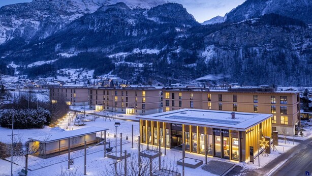 Un hôtel moderne doté d’un bâtiment central et d’une façade en verre, entouré de montagnes enneigées.