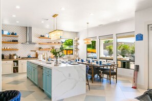 A modern kitchen with a marble island, wooden shelves, and a dining area with a view. - Sandbar/Lazy River/150K Gameroom (Indio)