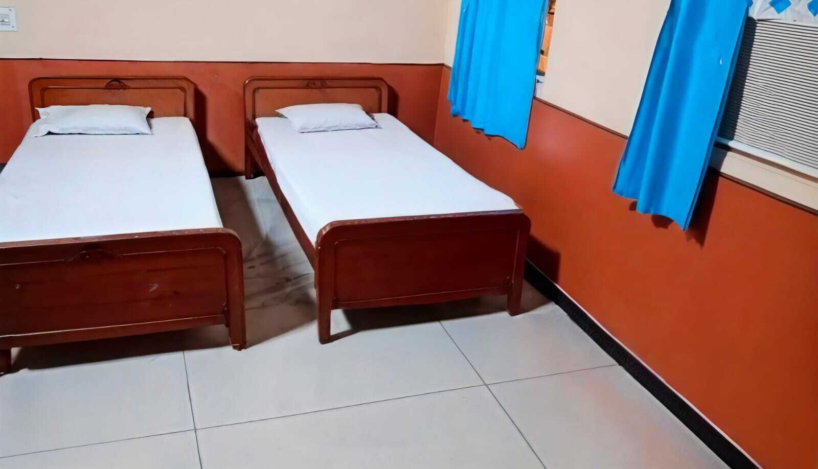 A room with two wooden beds, white bedding, orange walls, and blue curtains.