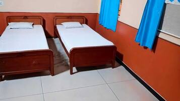 A room with two wooden beds, white bedding, orange walls, and blue curtains.