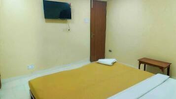 A room with a bed, a television mounted on the wall, a wooden door, and a small table.