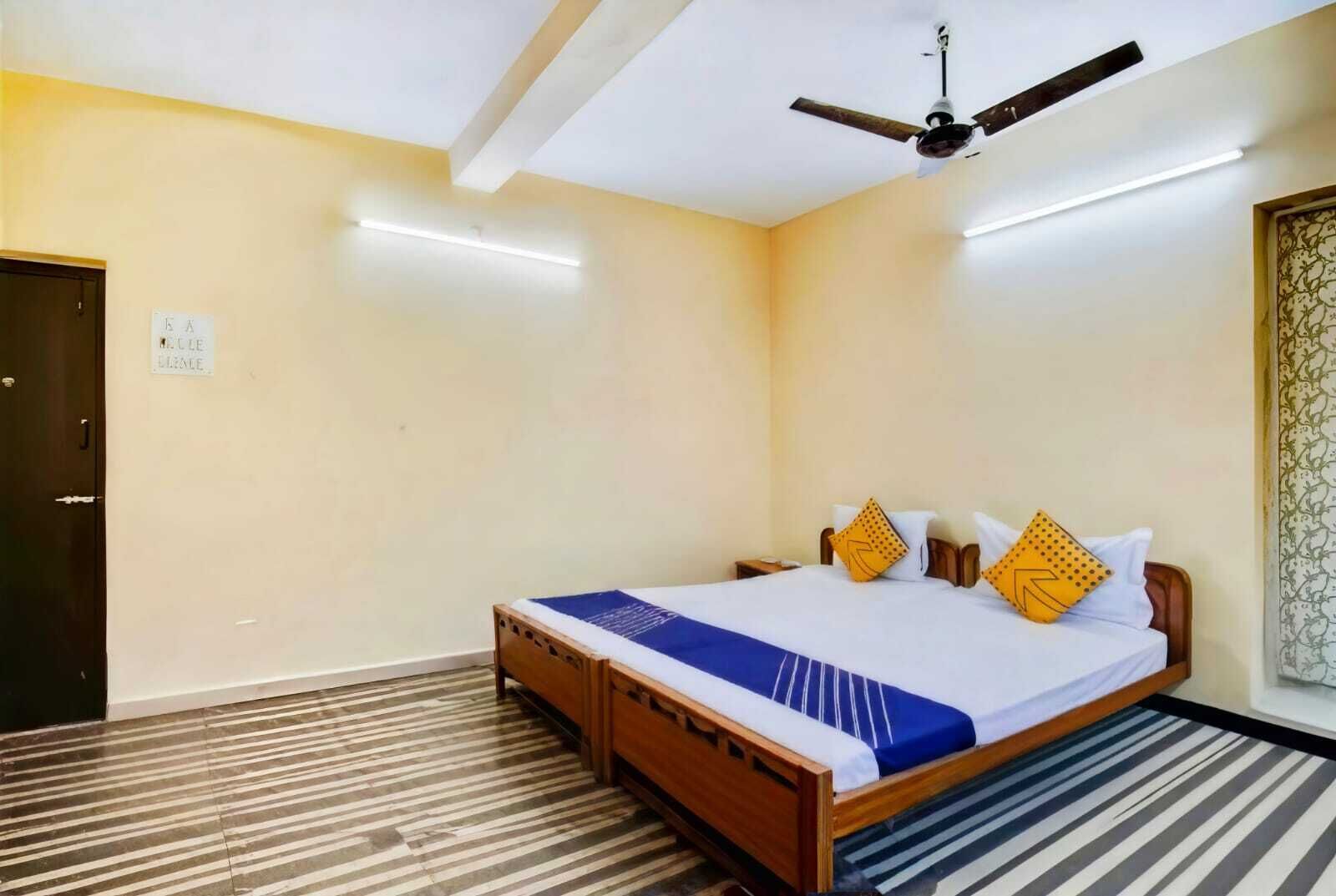 A hotel room with a bed, a ceiling fan, a door, and a sign on the wall.