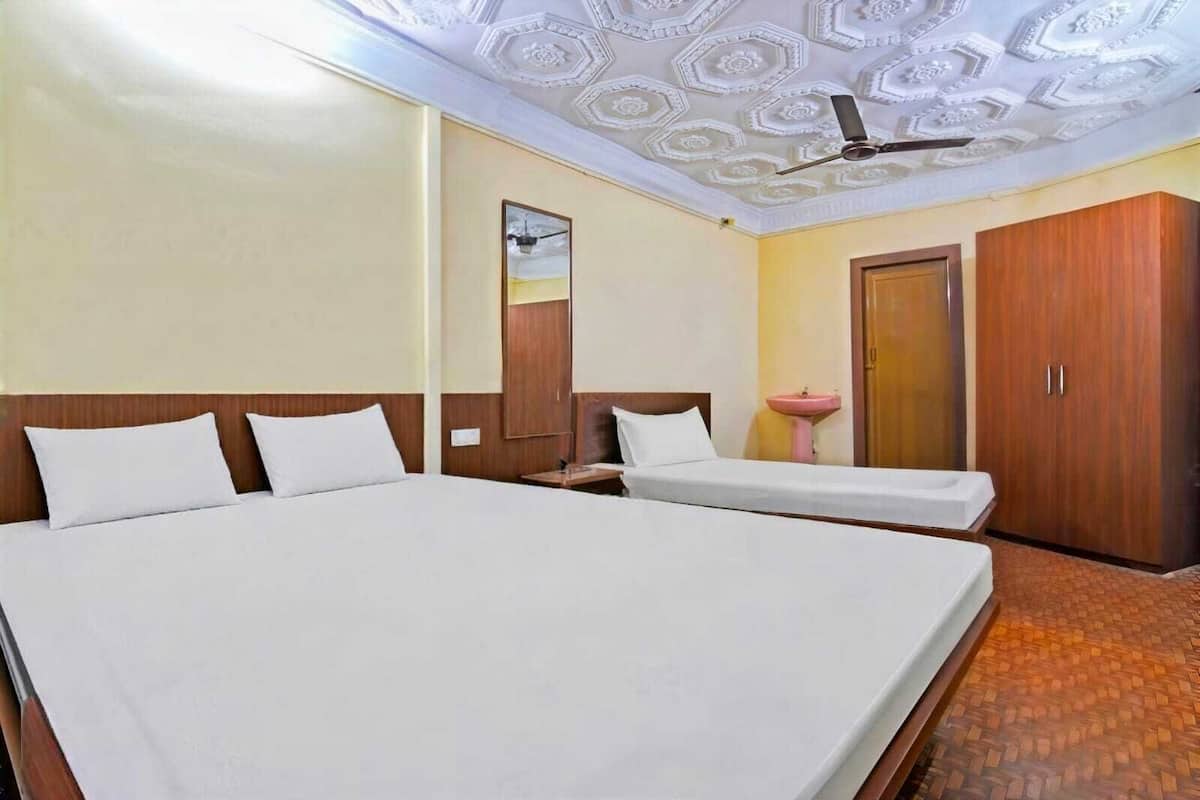 A hotel room with a large bed, a smaller bed, a ceiling fan, a mirror, a sink, and wooden wardrobes.