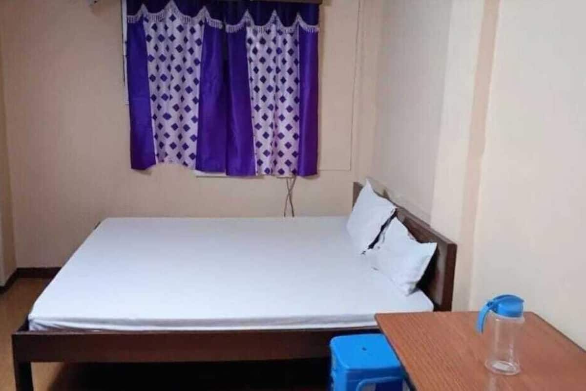 A single bed with a wooden frame, a small table with a blue container, and purple patterned curtains.