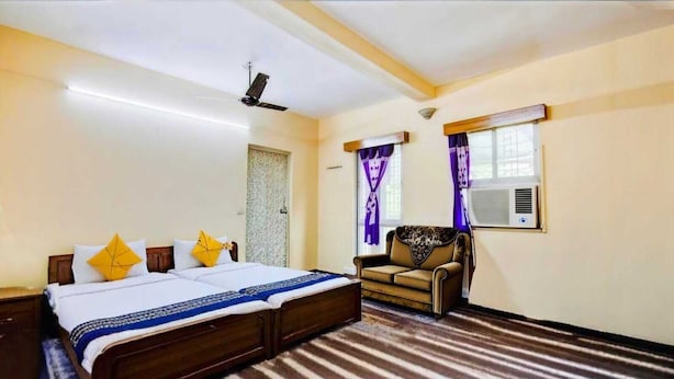 A bedroom with a bed, a sofa, a ceiling fan, and an air conditioning unit. - Dear Hotel (Kolkata)