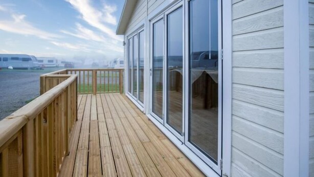 Terraza de madera con puerta de vidrio que da a un espacio exterior cubierto, con vista a un cuerpo de agua donde se ven barcos.