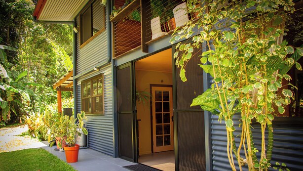 A modern house with a sliding glass door entrance, a small porch with potted plants, and a metal fence. - Luxury Rainforest Studio with Moroccan-Inspired Design & Lush Gardens (Kuranda)