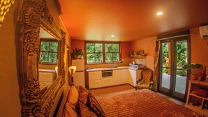 A bedroom with a large ornate mirror, a bed with a quilt, a dresser, and a window with a view of greenery. - Luxury Rainforest Studio with Moroccan-Inspired Design & Lush Gardens (Kuranda)