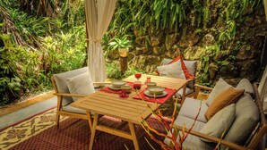 A wooden table set for two with chairs, a red table runner, and a backdrop of lush greenery and a rocky wall. - Luxury Rainforest Studio with Moroccan-Inspired Design & Lush Gardens (Kuranda)