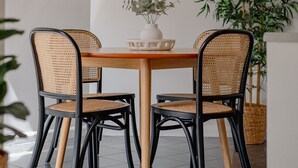 Un comedor con una mesa redonda, cuatro sillas, una lámpara colgante, un espejo y una planta en maceta.