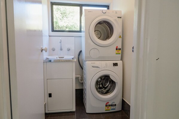 A laundry room with two stacked washing machines, a sink, and a window.