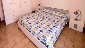 Ein Schlafzimmer mit Bett, Nachttisch, Schreibtisch, Kleiderschrank und Deckenleuchte.
