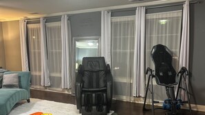 Ein Wohnzimmer mit Massagesessel, Trainingsgeräten, einem Korb für Yogamatten und einem türkisfarbenen Sofa.