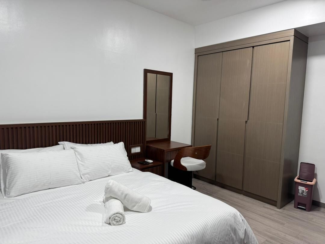 Ein Hotelzimmer mit Bett, Schreibtisch, Stuhl, Kleiderschrank und Mülleimer.