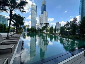Una piscina con sillas de descanso, rodeada de edificios altos y palmeras.