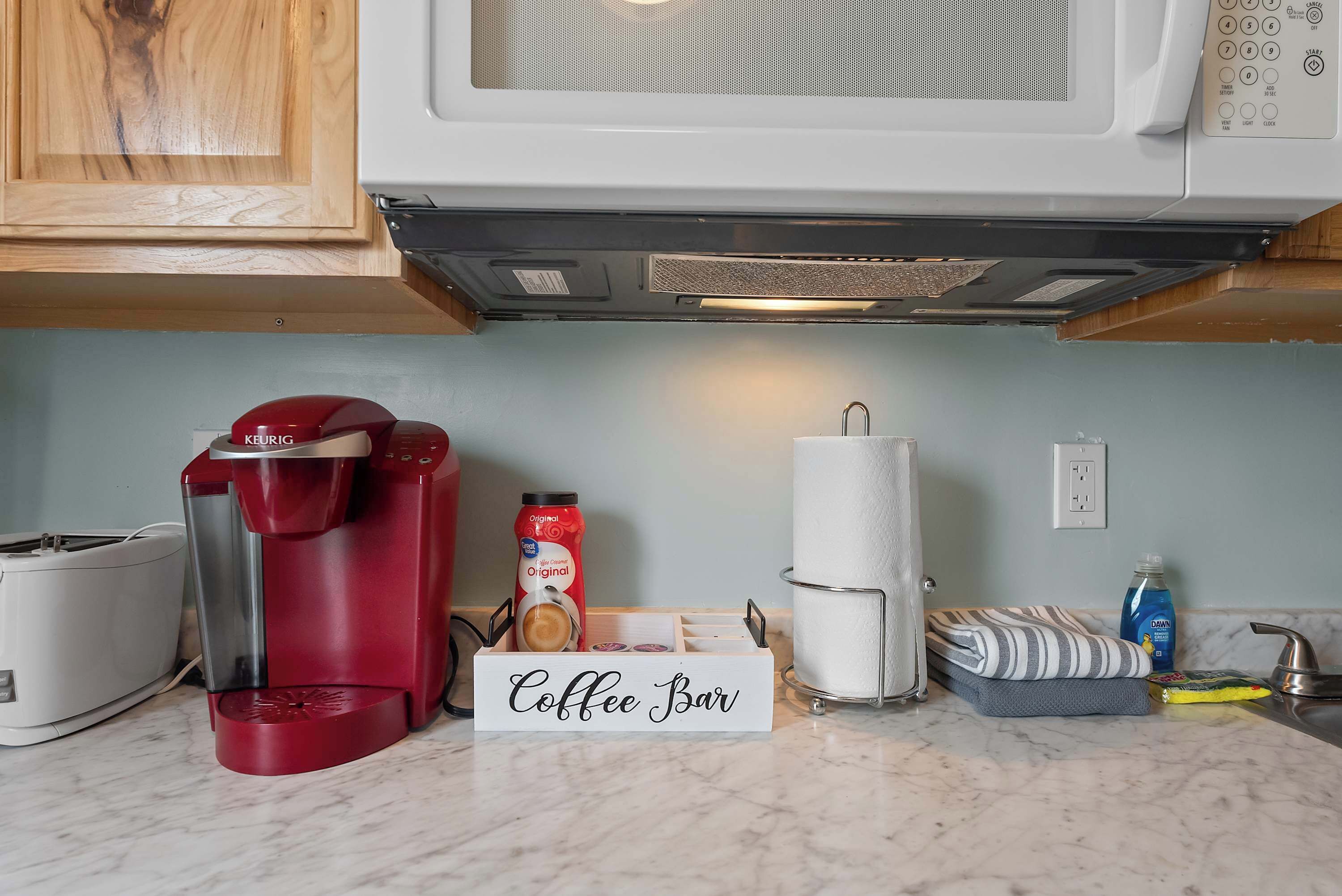 Une cuisine équipée d’une machine à café, d’un four à micro-ondes, d’un grille-pain et d’un panneau indiquant un espace dédié à la préparation du café.