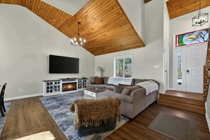 Un salon avec un plafond en bois, une cheminée, un canapé, un téléviseur et une porte ornée d’un vitrail.