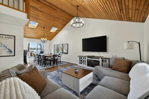 Un salon moderne doté d’un plafond en bois, d’un téléviseur à écran plat, d’une cheminée et d’un coin repas avec une table et des chaises.