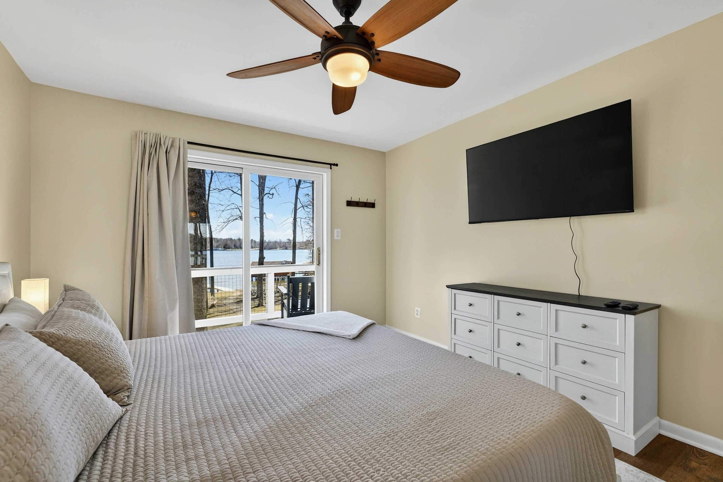 Upper Bedroom - A wall-mounted TV and dresser round out the room, with lake and deck views through the sliding door.