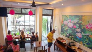 Spiseområde med borde, stole, en person der serverer mad, og et stort blomster maleri på væggen.