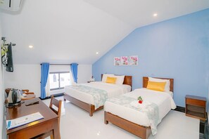 Ein Hotelzimmer mit zwei Betten, einem Schreibtisch mit Stuhl, einem kleinen Tisch und einem Fenster mit Vorhängen.