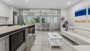 A modern kitchen with a dining area, white furniture, and a view through glass doors. - Coastal Calm at Paradiso - 231 (Tweed)