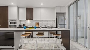 A modern kitchen with white cabinets, a large island with bar stools, a microwave, and a refrigerator. - Coastal Calm at Paradiso - 231 (Tweed)