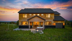 A modern two-story house with a covered porch, a fire pit, and a view of the landscape.