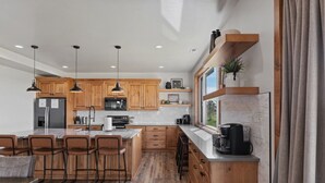 A modern kitchen with wooden cabinets, a central island with bar stools, a built-in microwave, and a coffee machine.