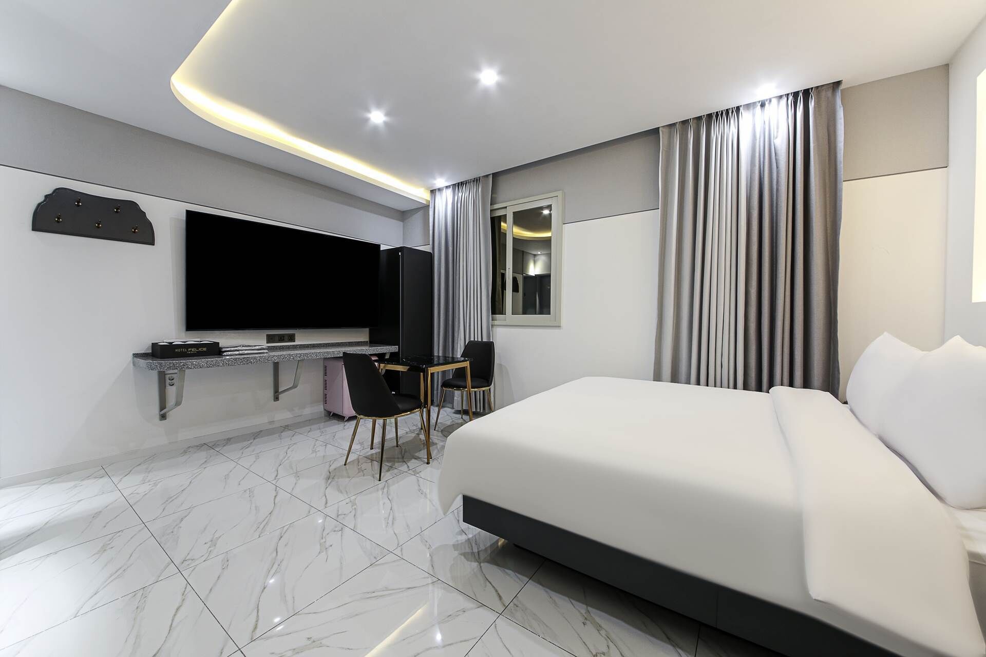 Habitación de hotel moderna con una cama grande, televisor de pantalla plana, escritorio con computadora y espejo de baño.