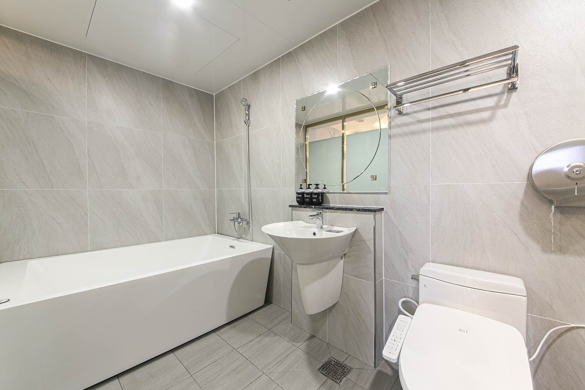 Ein modernes Badezimmer mit Badewanne, Waschbecken, Toilette und einem Spiegel mit Handtuchhalter.