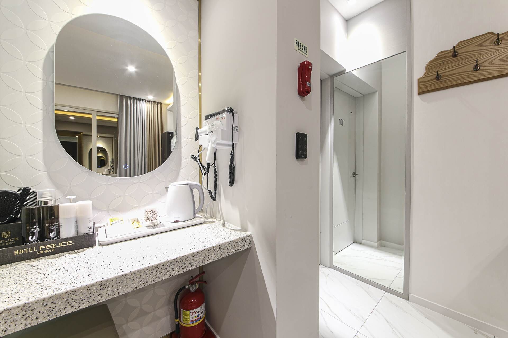 Un baño moderno con un espejo grande, un secador de pelo, una cafetera y un extintor.