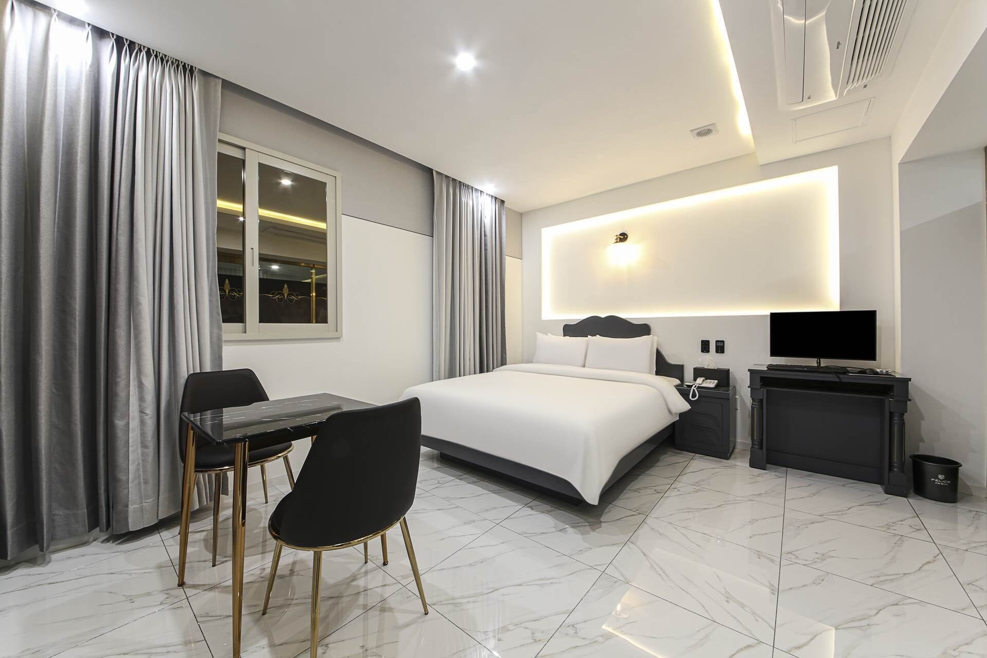 A modern hotel room with a bed, a desk, a chair, a TV, and a bathroom.